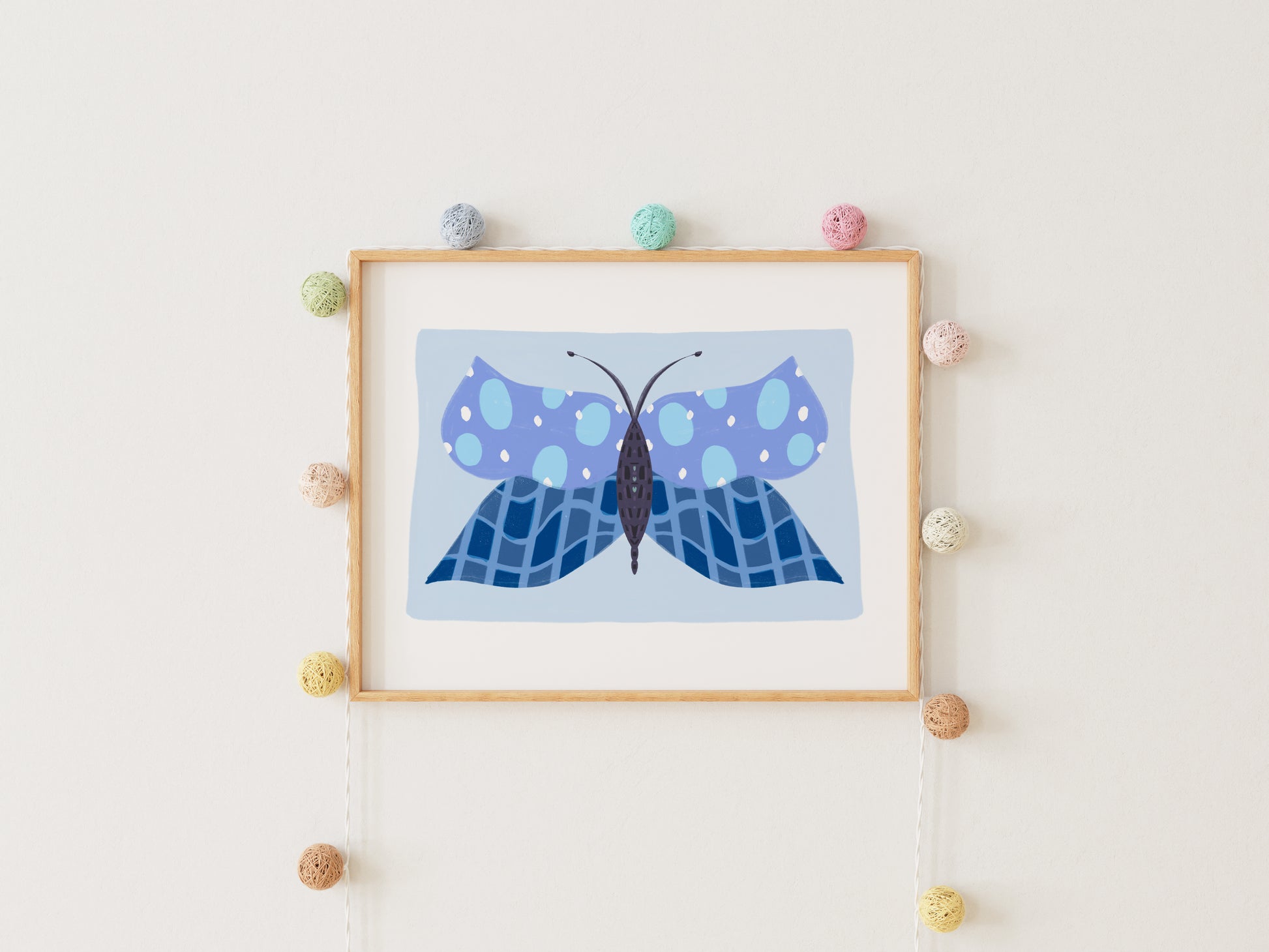 Framed artwork of a blue butterfly on a white wall with decorative pom-poms.