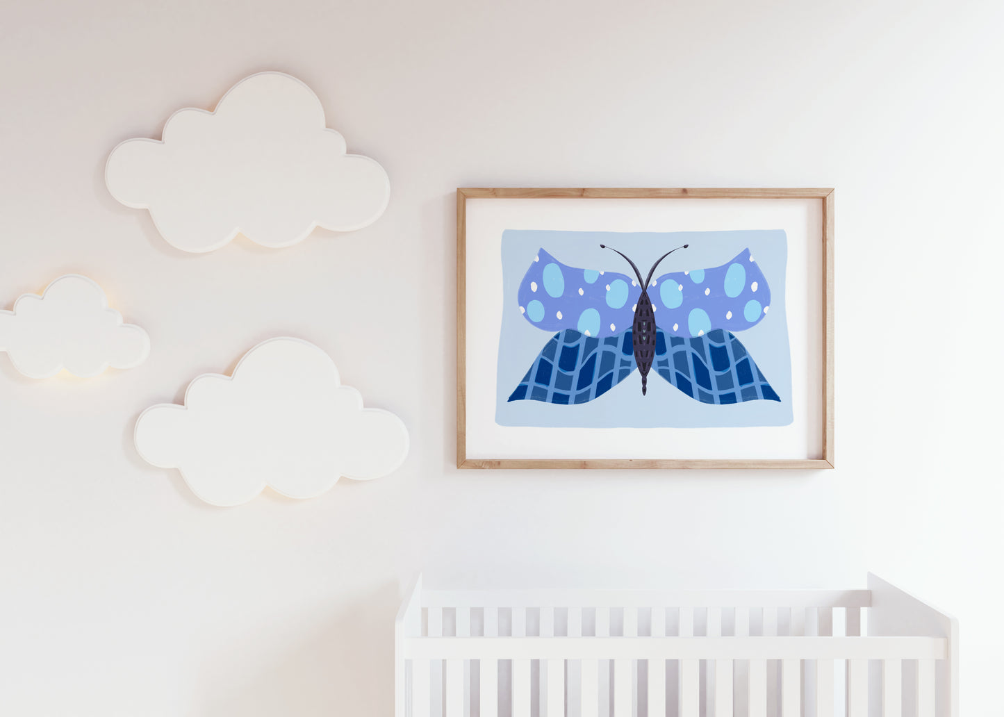Framed blue butterfly artwork on a wall above a crib in a nursery.