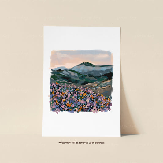 Blue mountain landscape print featuring layered green hills, colourful foreground wildflowers and a soft peach sky
