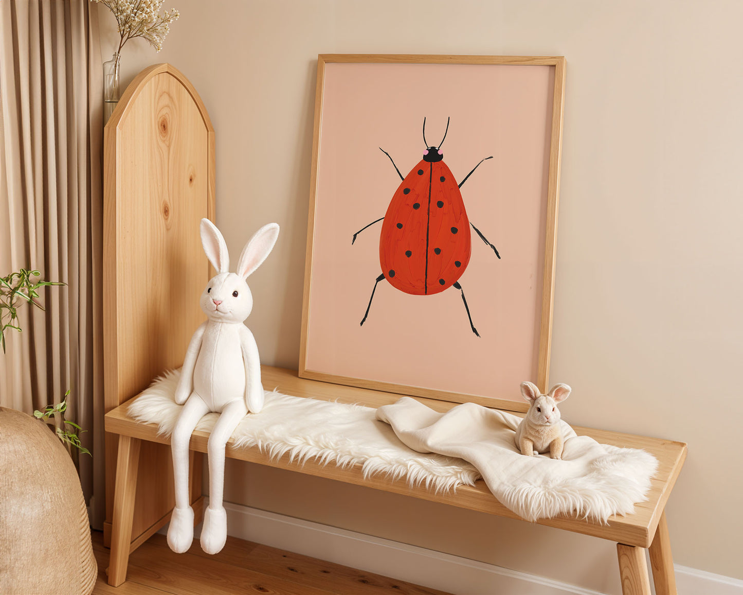 Wooden bench with plush toys and a framed illustration of a red ladybug on a beige wall.