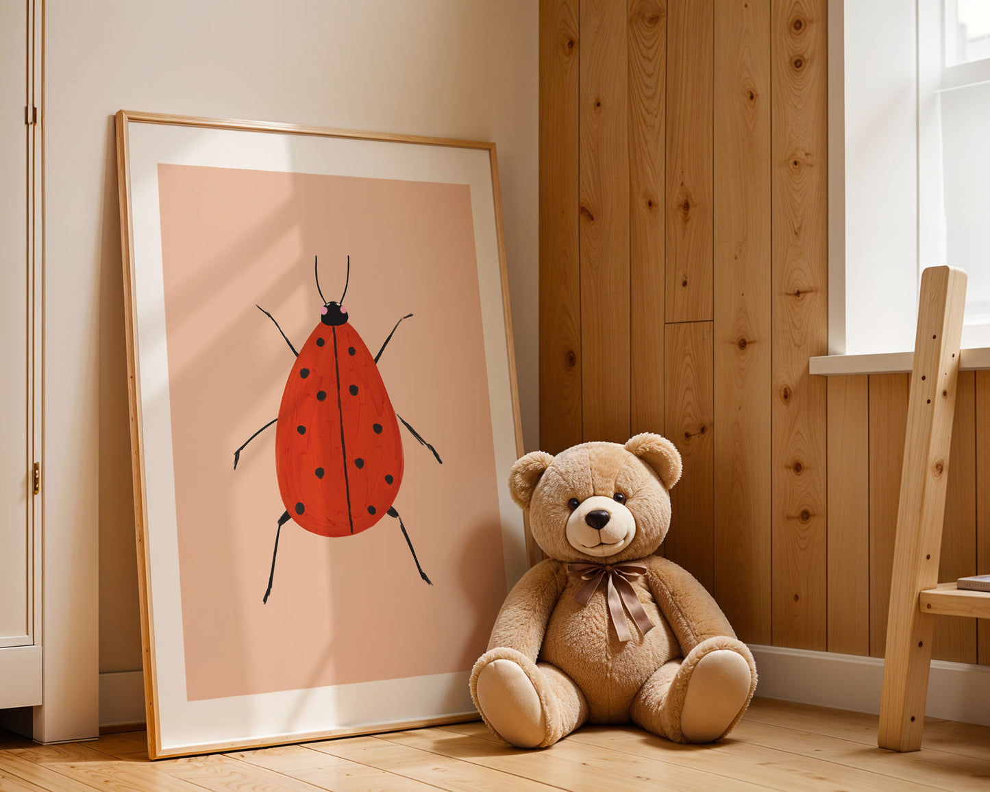 Teddy bear sitting next to a framed illustration of a red ladybug on a wooden floor.