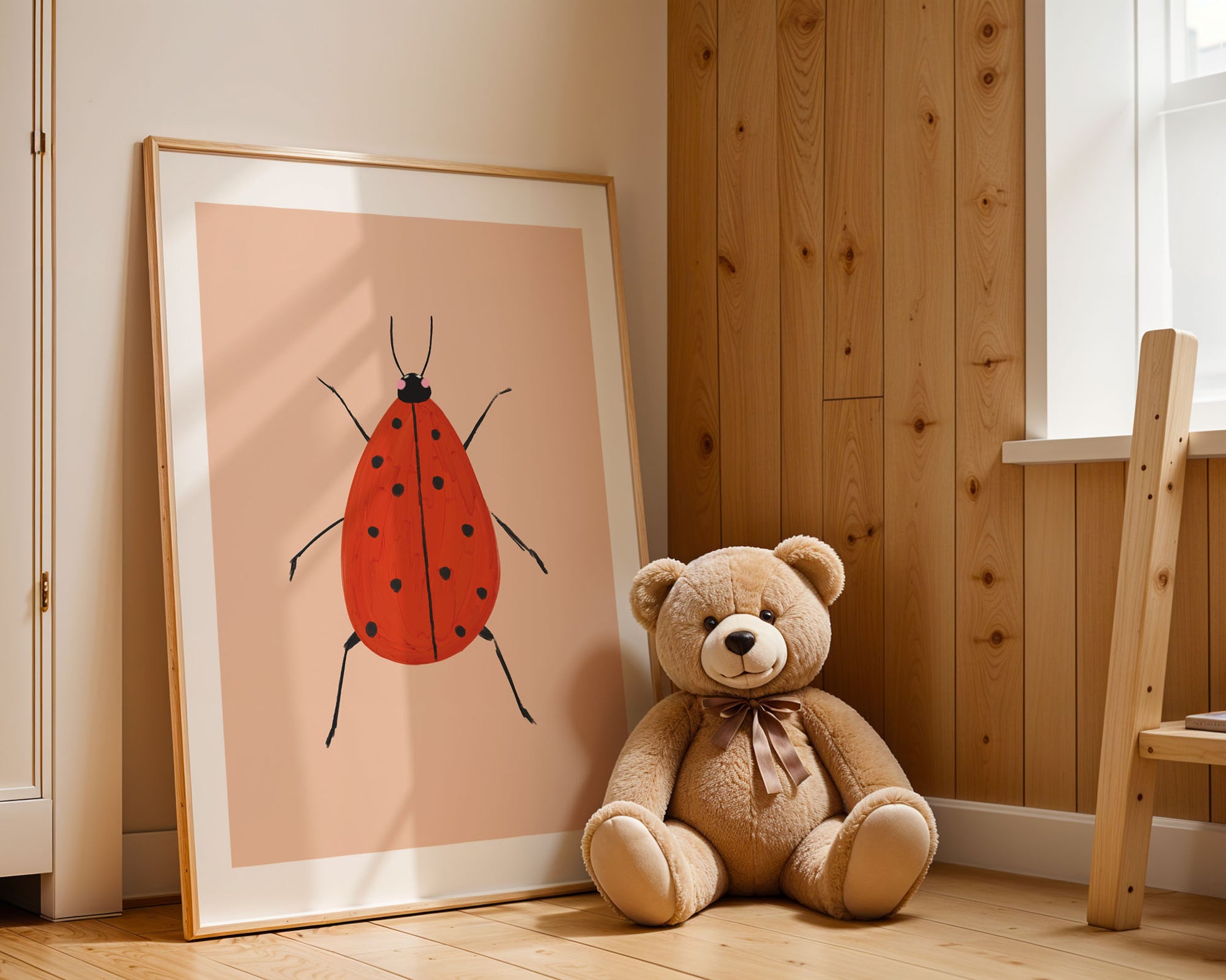 Teddy bear sitting next to a framed illustration of a red ladybug on a wooden floor.