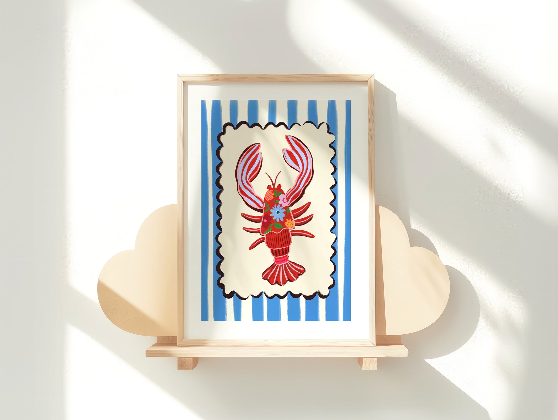 Framed artwork of a red lobster on a blue and white striped background, displayed on a wooden stand.