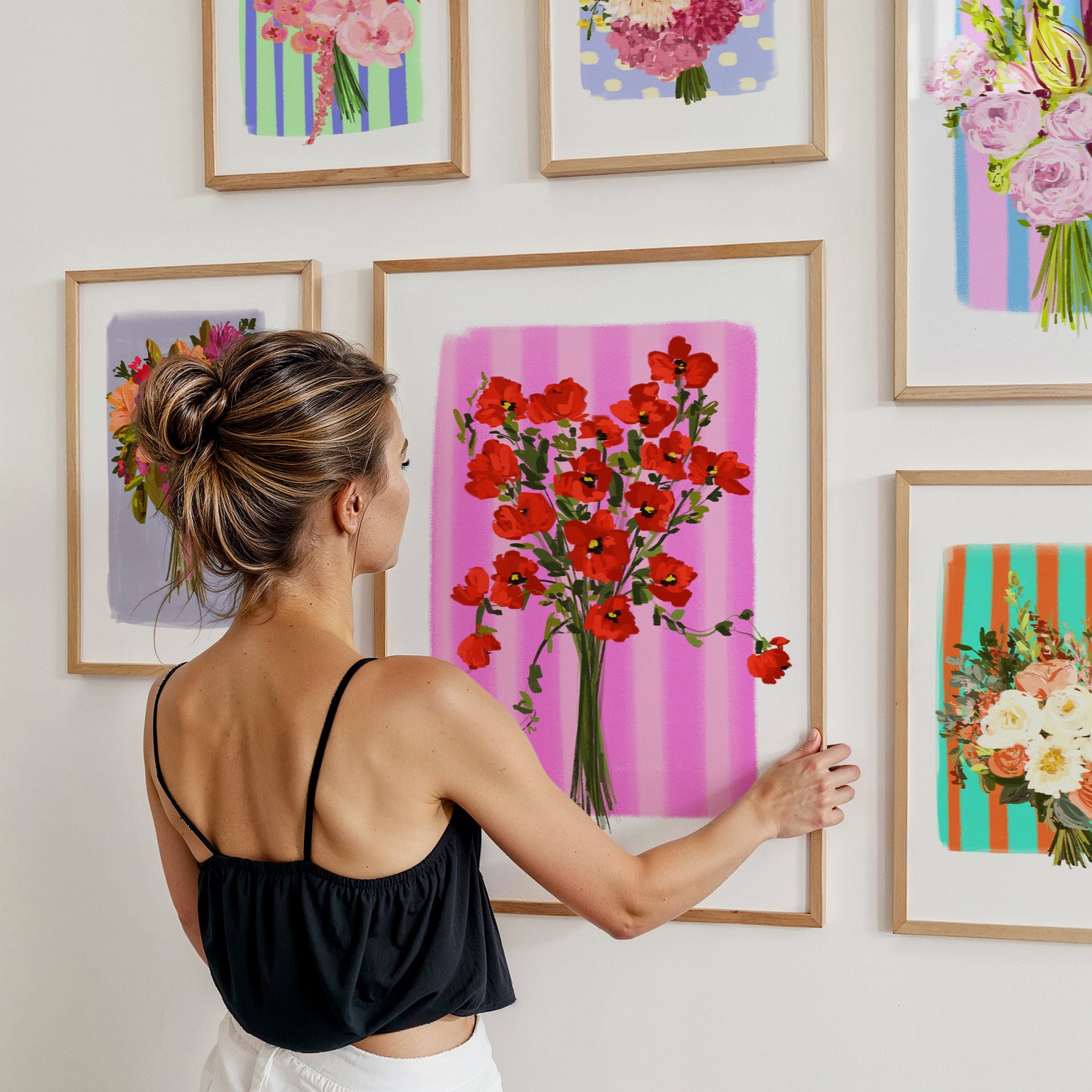 Woman arranging floral art prints on a wall